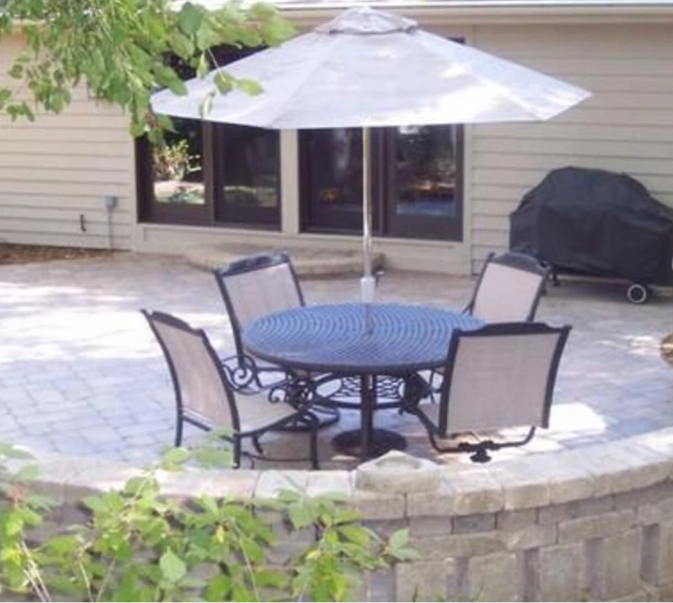 A beige sided house with a large patio featuring a round table, four chairs, and a white umbrella.